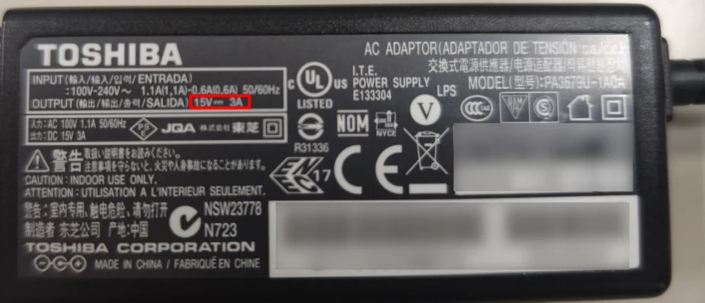 ノートパソコンのACアダプターの「レンガ」のような四角い部分。その裏面の細かい文字の中に「OUTPUT」という表記がある様子。