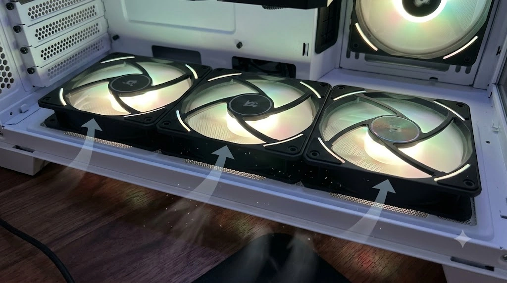 PCケース底面のメッシュフィルターに取り付けられた3基の通常ケースファン。内側（上）を向いたファンの裏面には、モーターを支える黒いフレームと配線が見える。ファン側面には、空気が下から上へ（ケース外から内へ）流れていることを示す、テキストなしの矢印が描かれている。